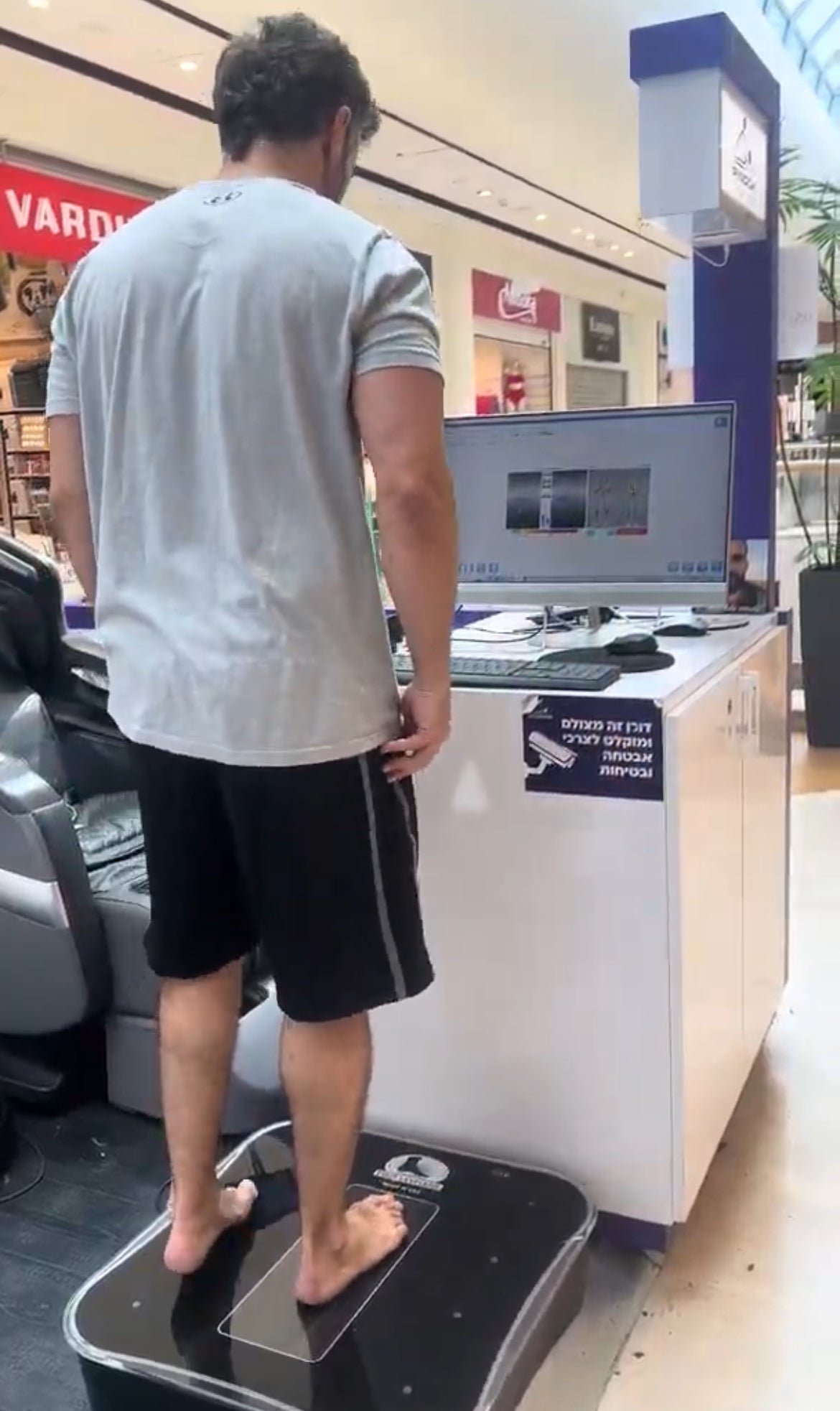 אדם משתמש במכשיר עיסוי לגב לשיקום מפציעה ובכאבי גב תחתון בקניון.